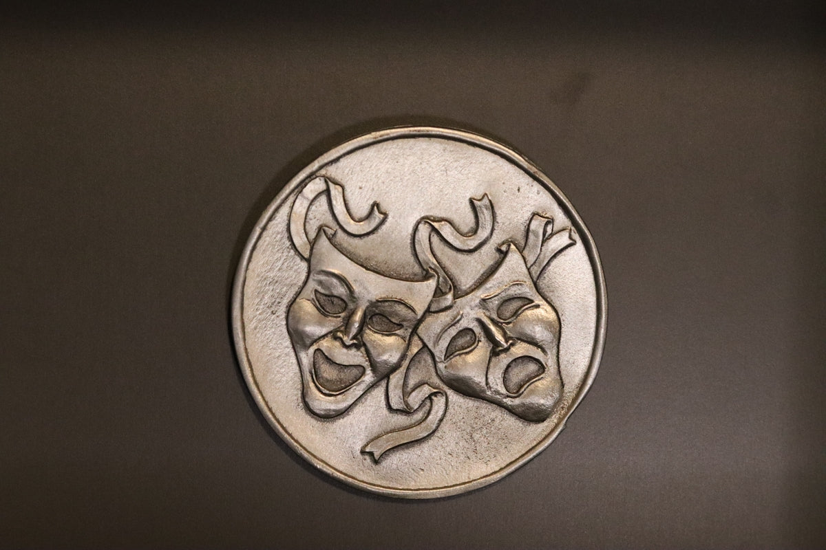 a metal medallion with two masks on it