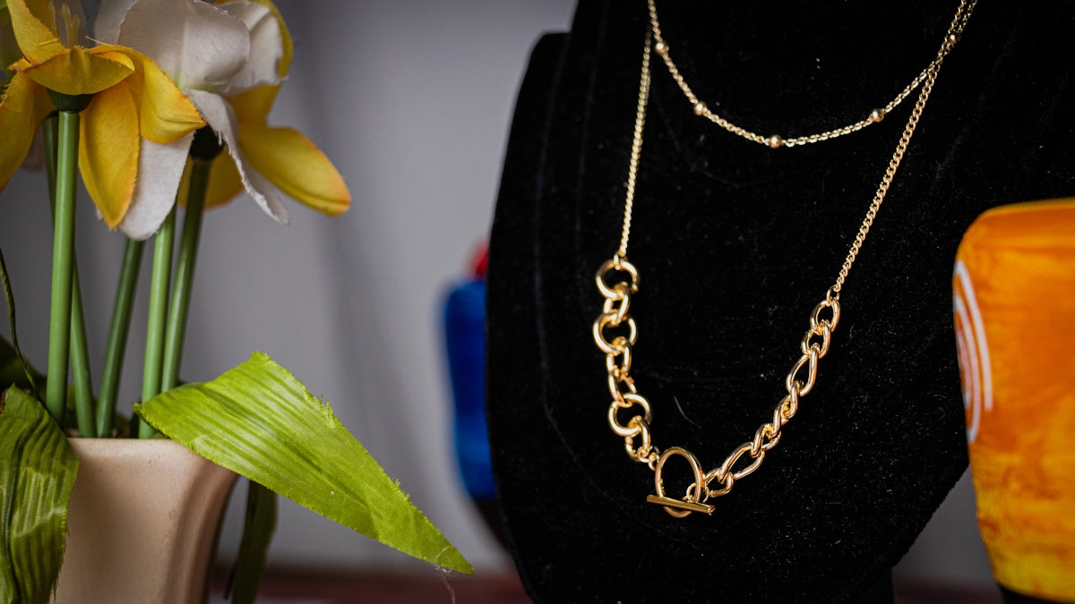 a gold necklace on a mannequin next to a vase with flowers
