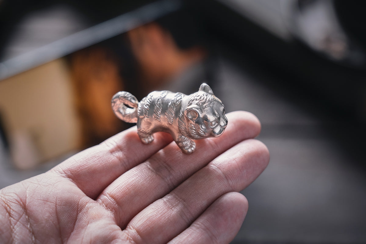 a small silver cat figurine sitting on top of a person's hand