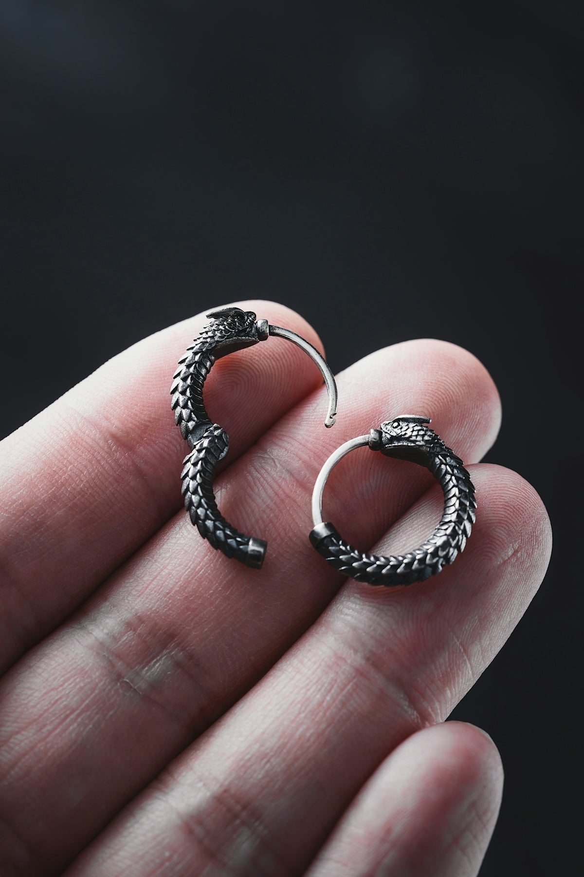 a hand holding a pair of silver hoop earrings
