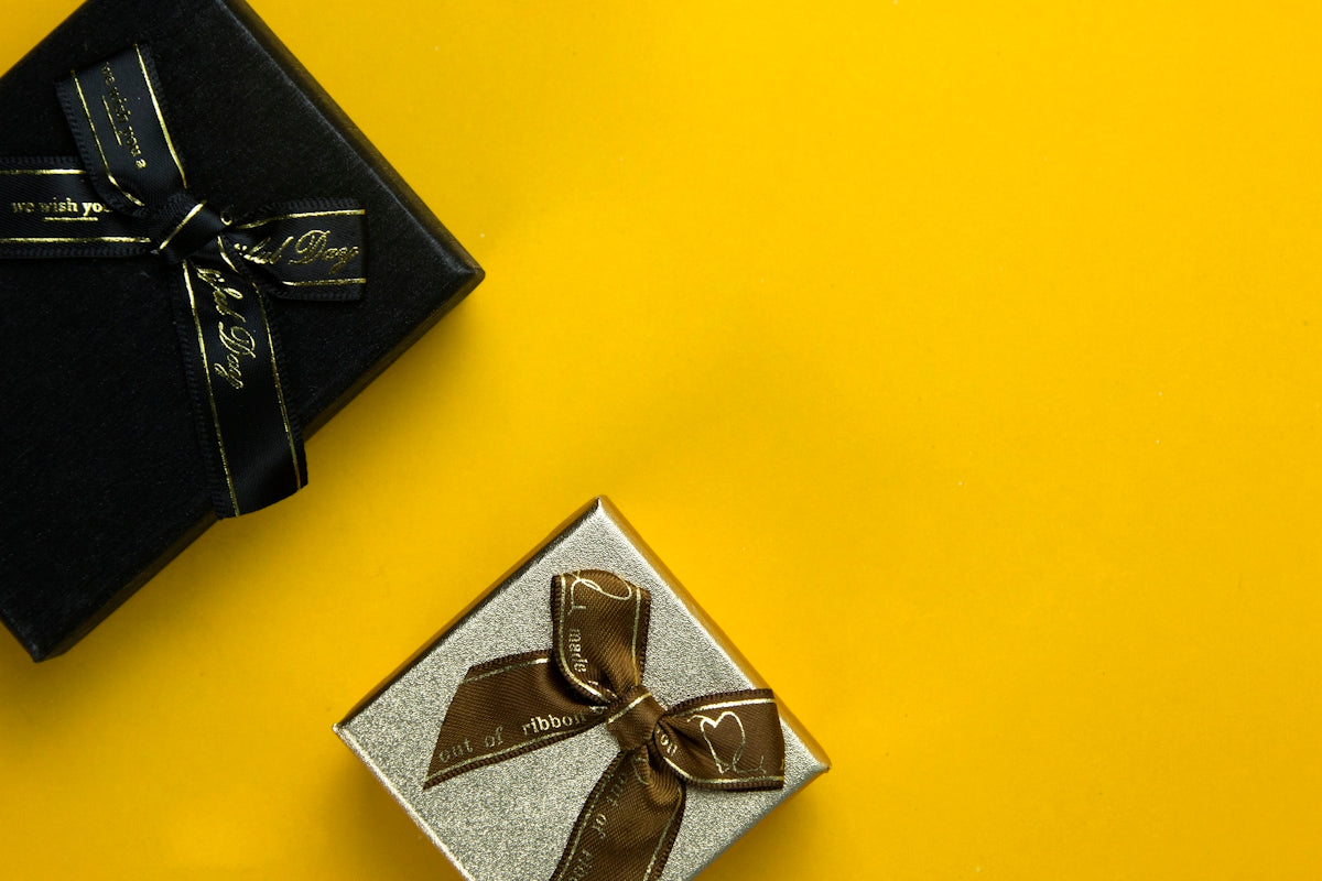 a black box with a gold ribbon and a silver box with a brown bow