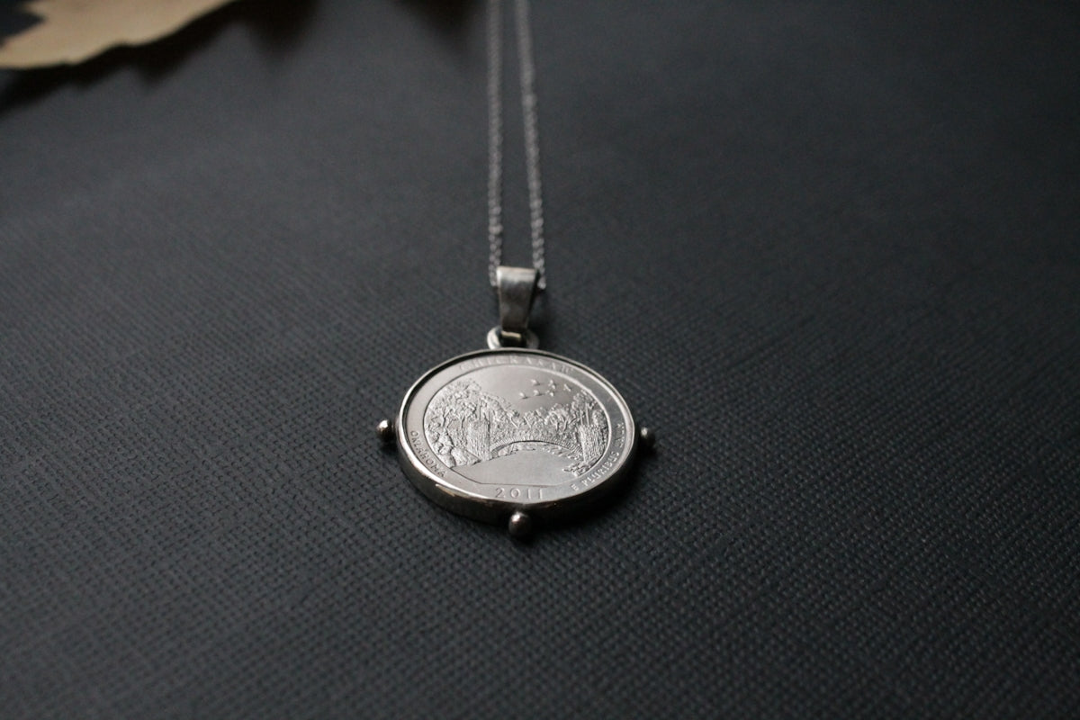 a small silver coin on a chain on a black surface