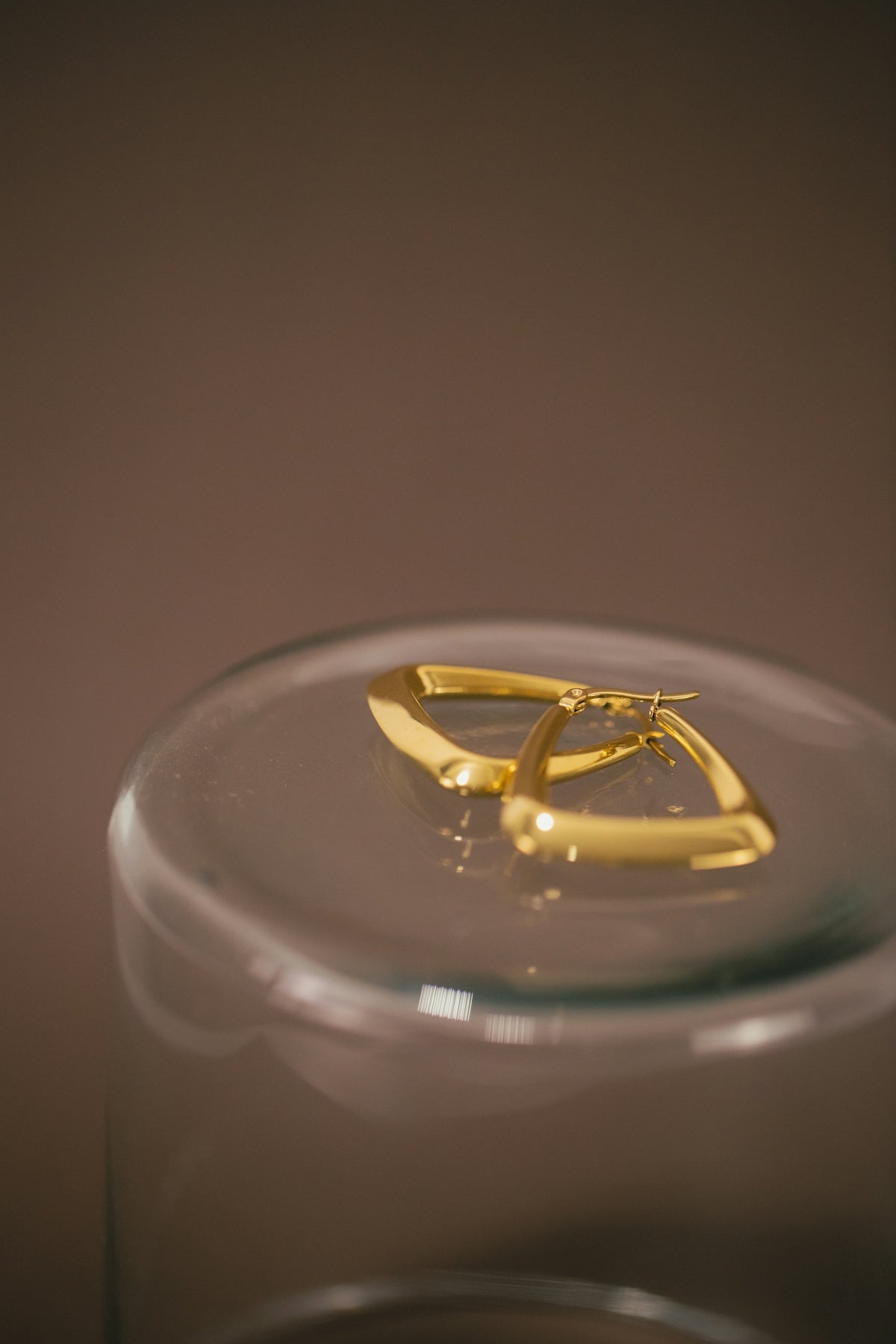 a pair of gold earrings sitting on top of a glass container