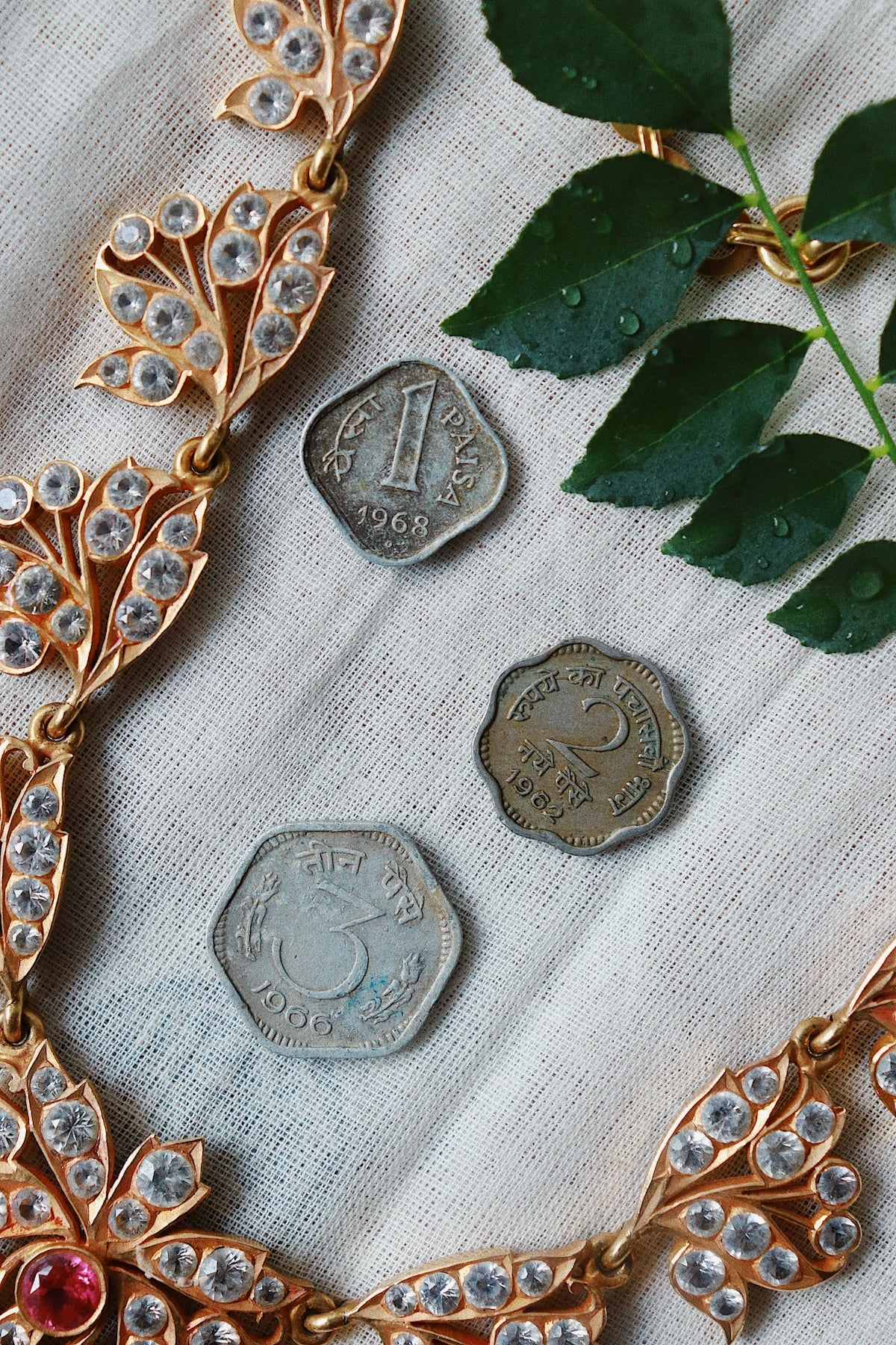 Jewelry, coins, and leaves arranged on a white cloth.