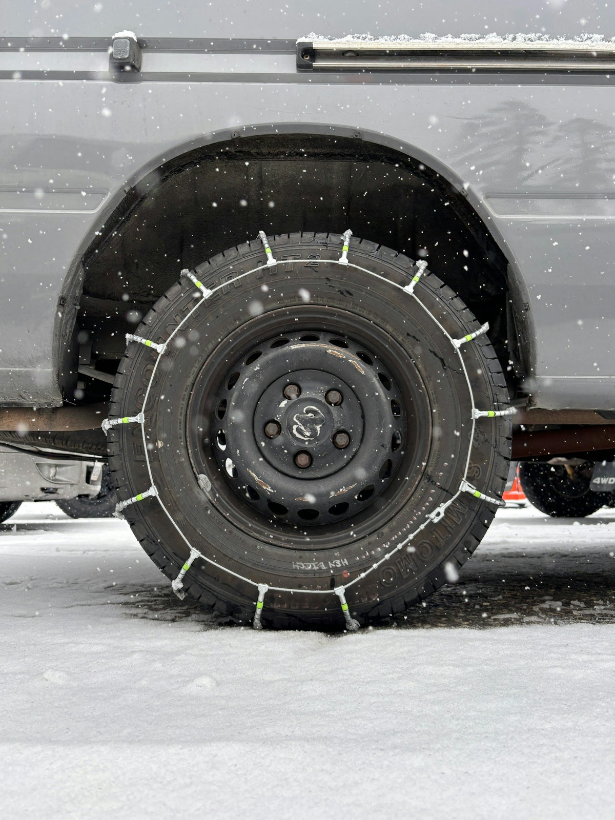 Snow chains are on a car tire in snow.