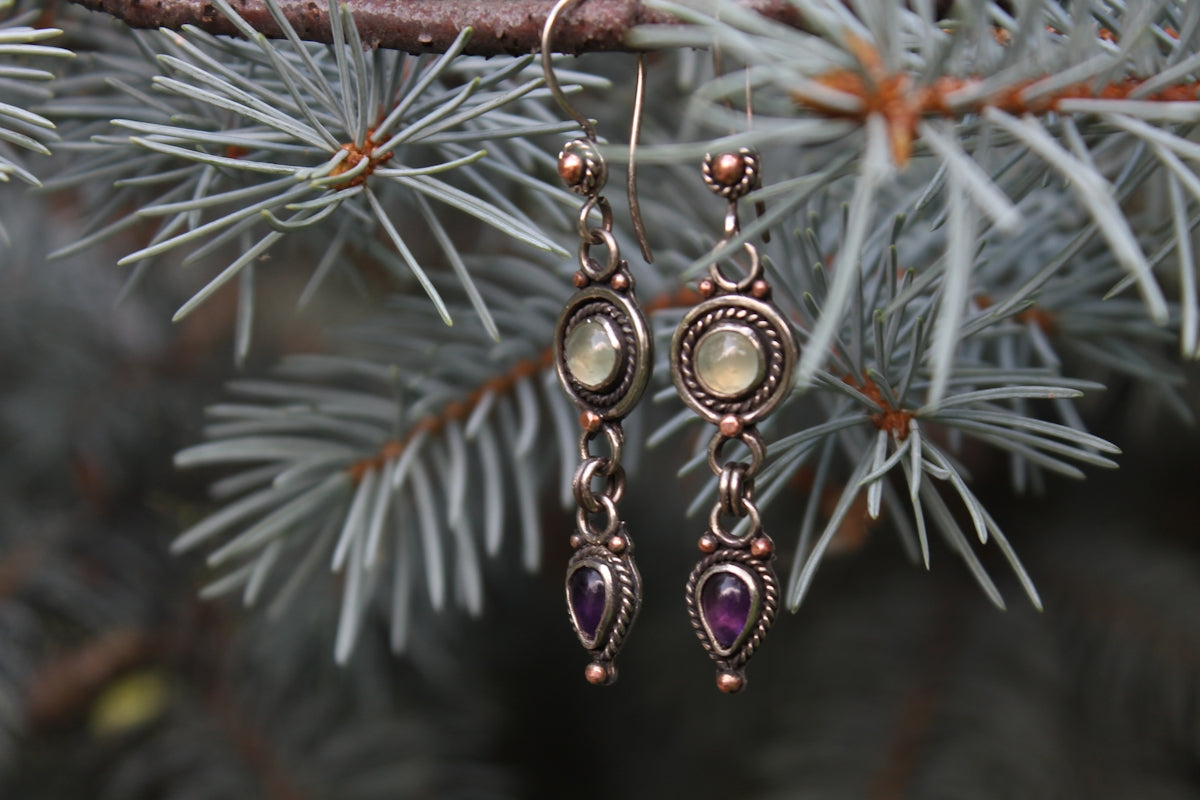 Elegant earrings hang against a soft, blurry background.