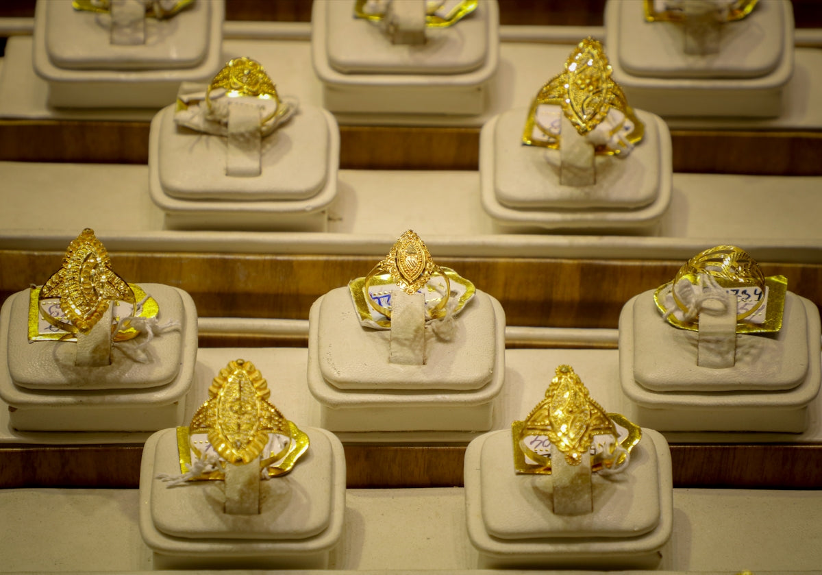 Several ornate gold rings displayed on white stands.