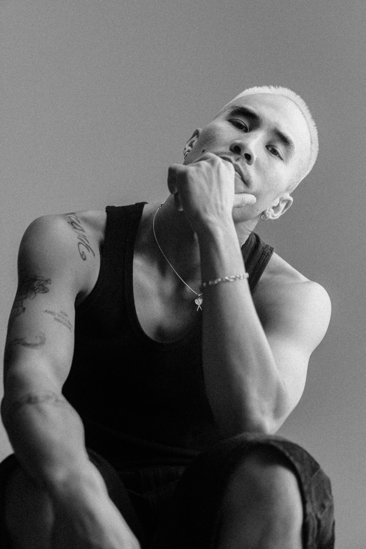Man with bleached hair wearing tank top and jewelry.