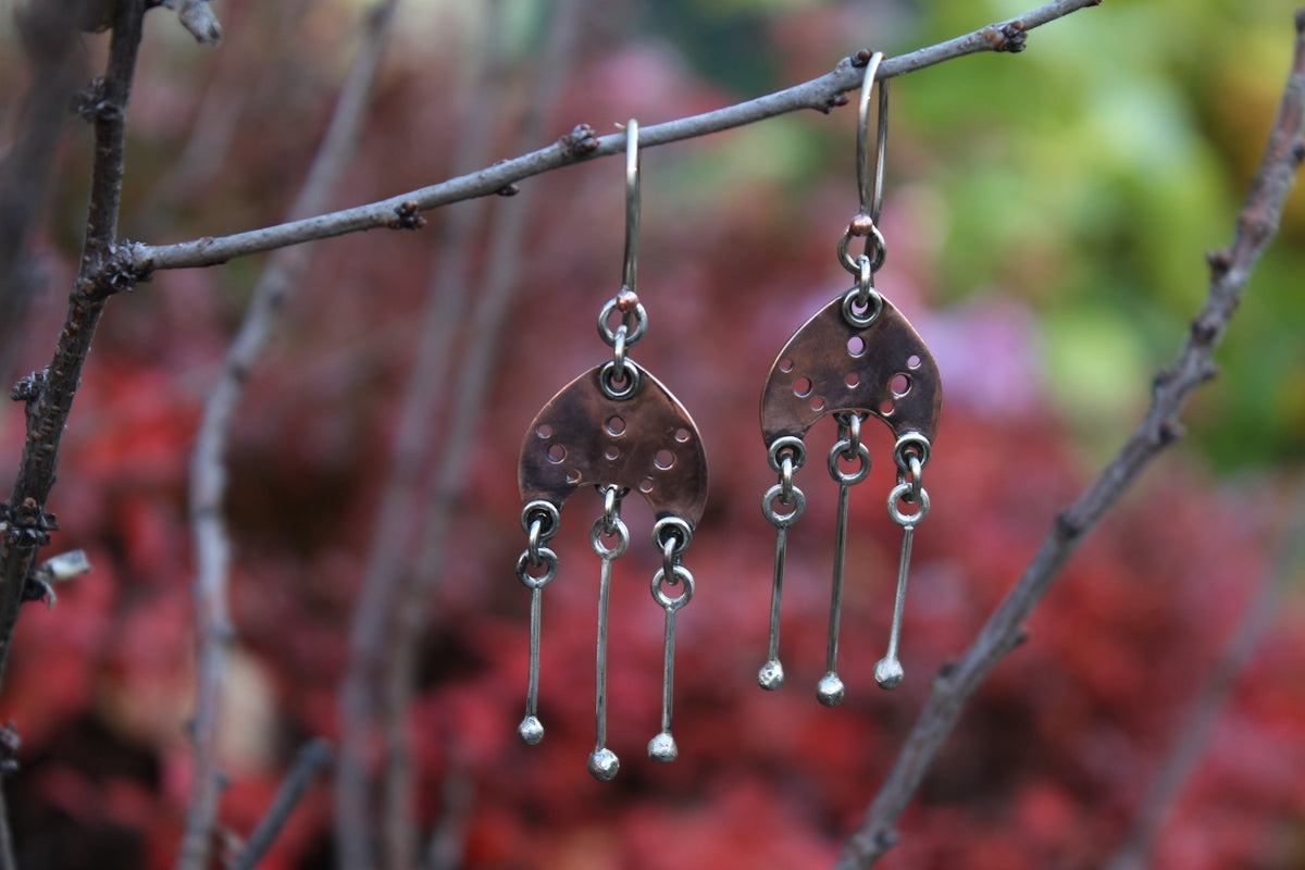 Handmade silver earrings hanging from a branch.