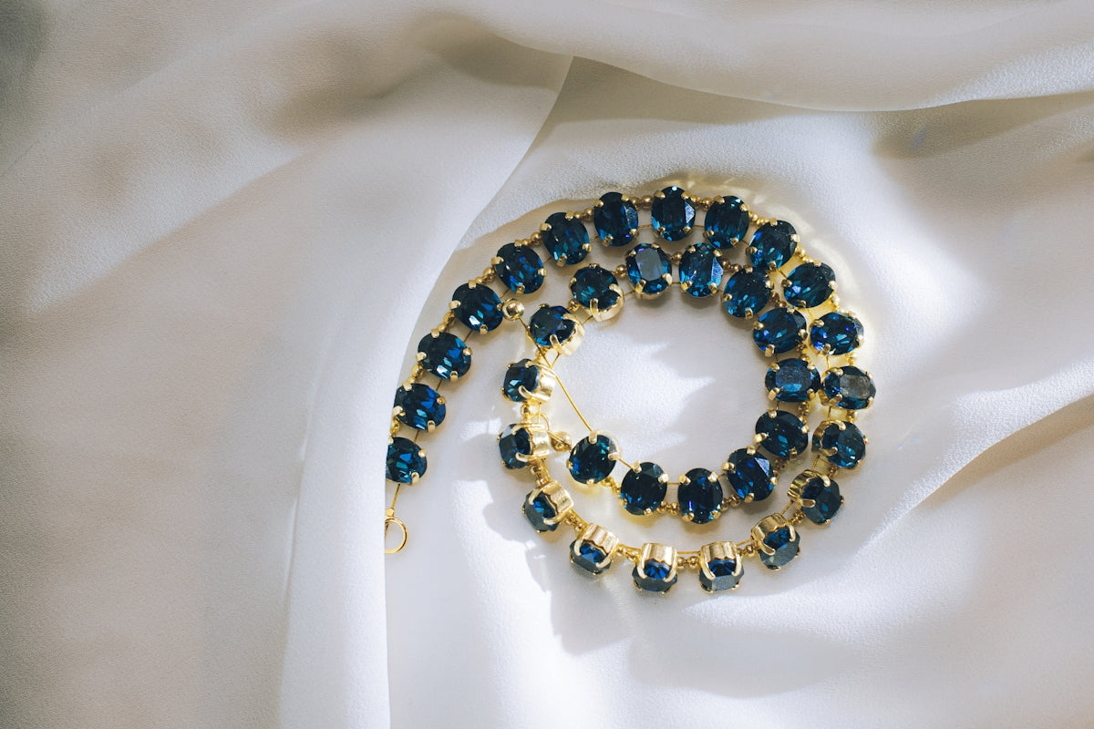 Gold necklace with dark blue gemstones on white satin